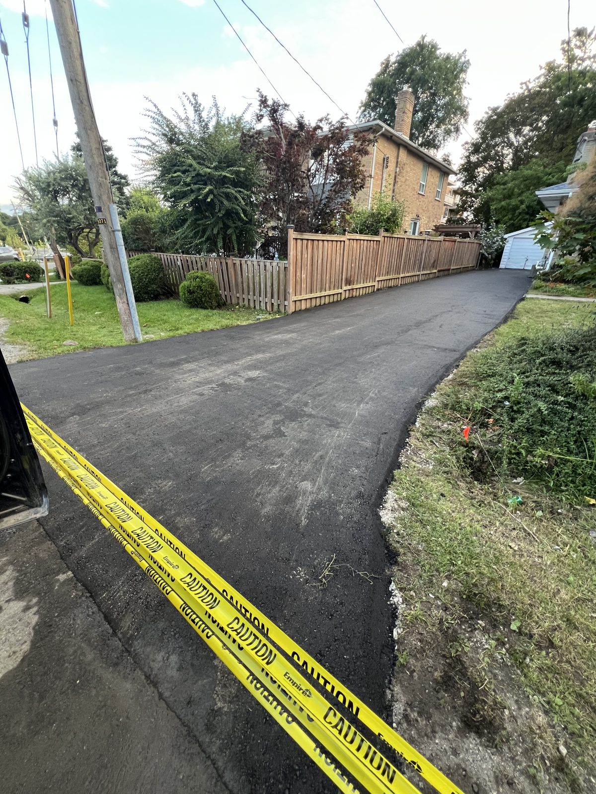Newly paved residential asphalt driveway lined with a wooden fence and caution tape in the Greater Toronto Area