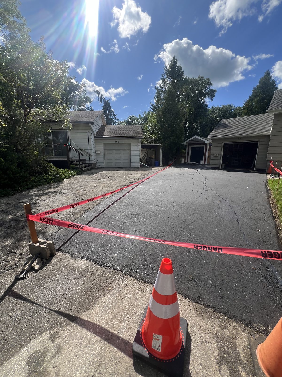 Newly paved asphalt driveway in the GTA sealed off with danger tape and safety cone while curing between two garages