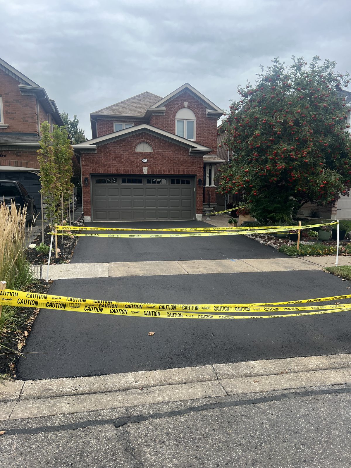 Newly paved asphalt driveway with caution tape at a brick home in the GTA, showing a smooth black finish