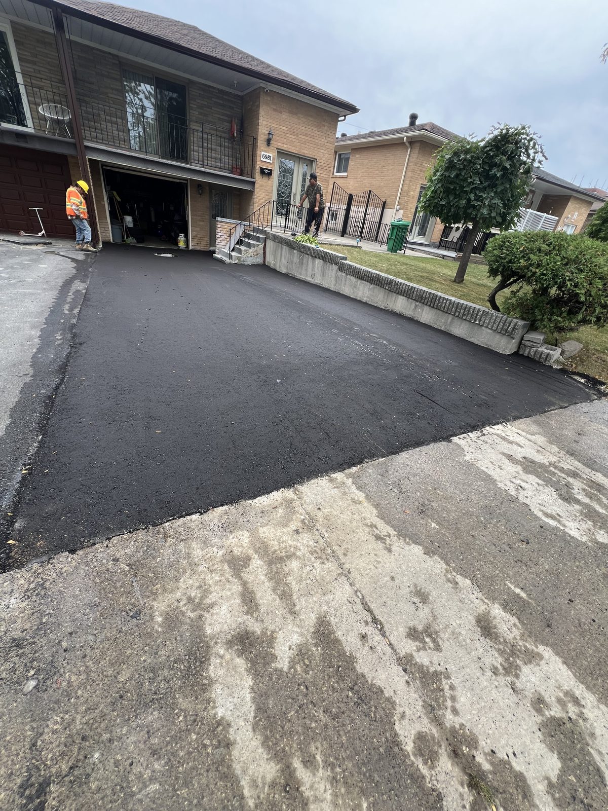 Newly paved smooth asphalt driveway leading to a GTA home garage with a paving crew member on site