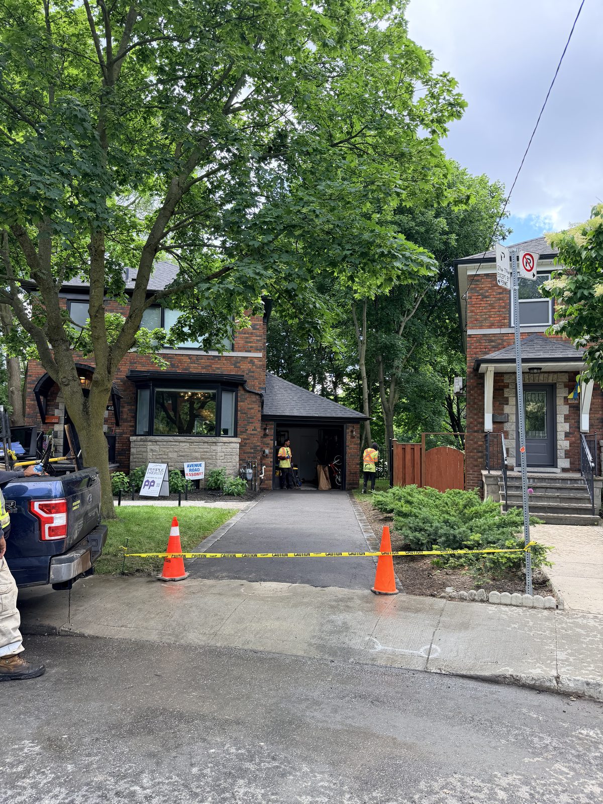 Newly paved asphalt driveway between two brick homes with caution tape, cones and crew working in the Toronto GTA
