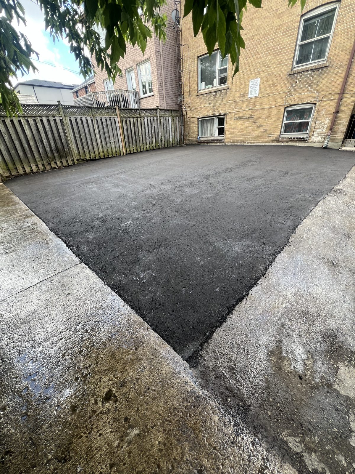 Freshly paved asphalt backyard parking area meeting concrete pads behind a brick building in the GTA