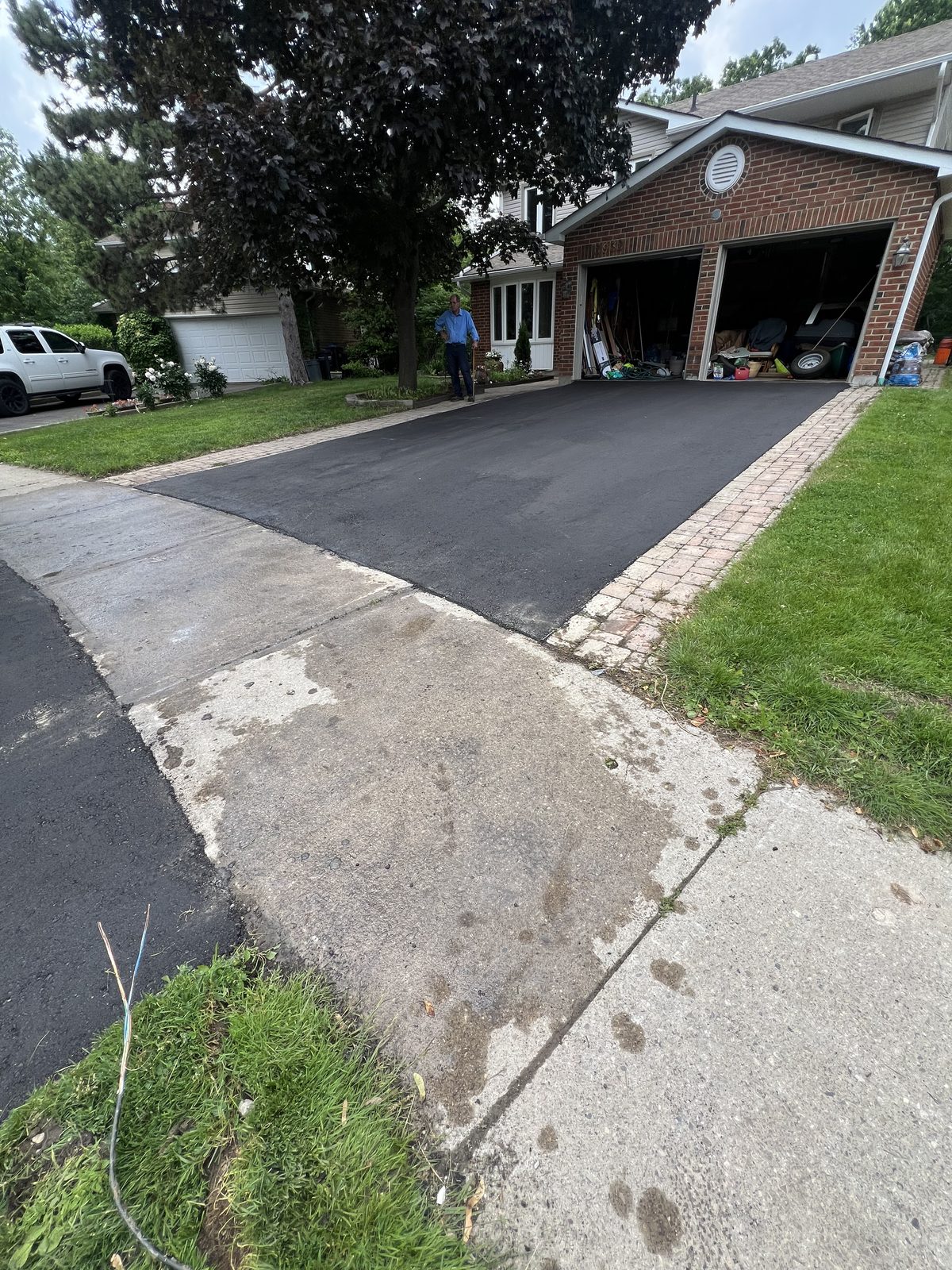 Newly paved asphalt driveway with decorative paver border leading to a two-car garage at a GTA home