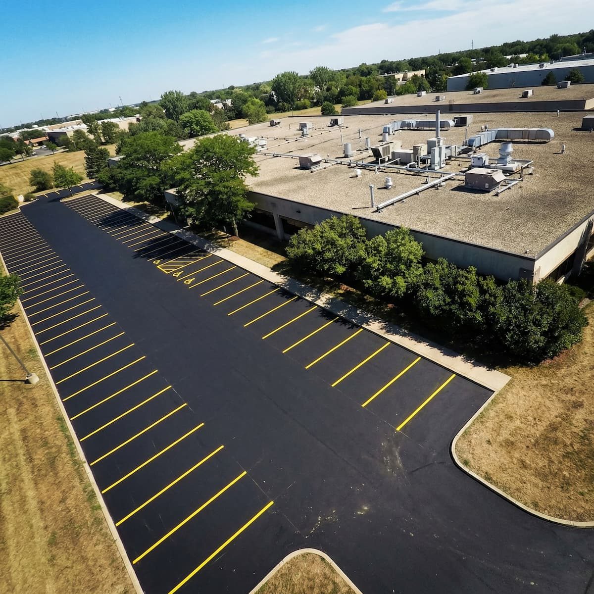 Aerial view of a newly paved asphalt parking lot with crisp yellow line striping beside a commercial building in the GTA