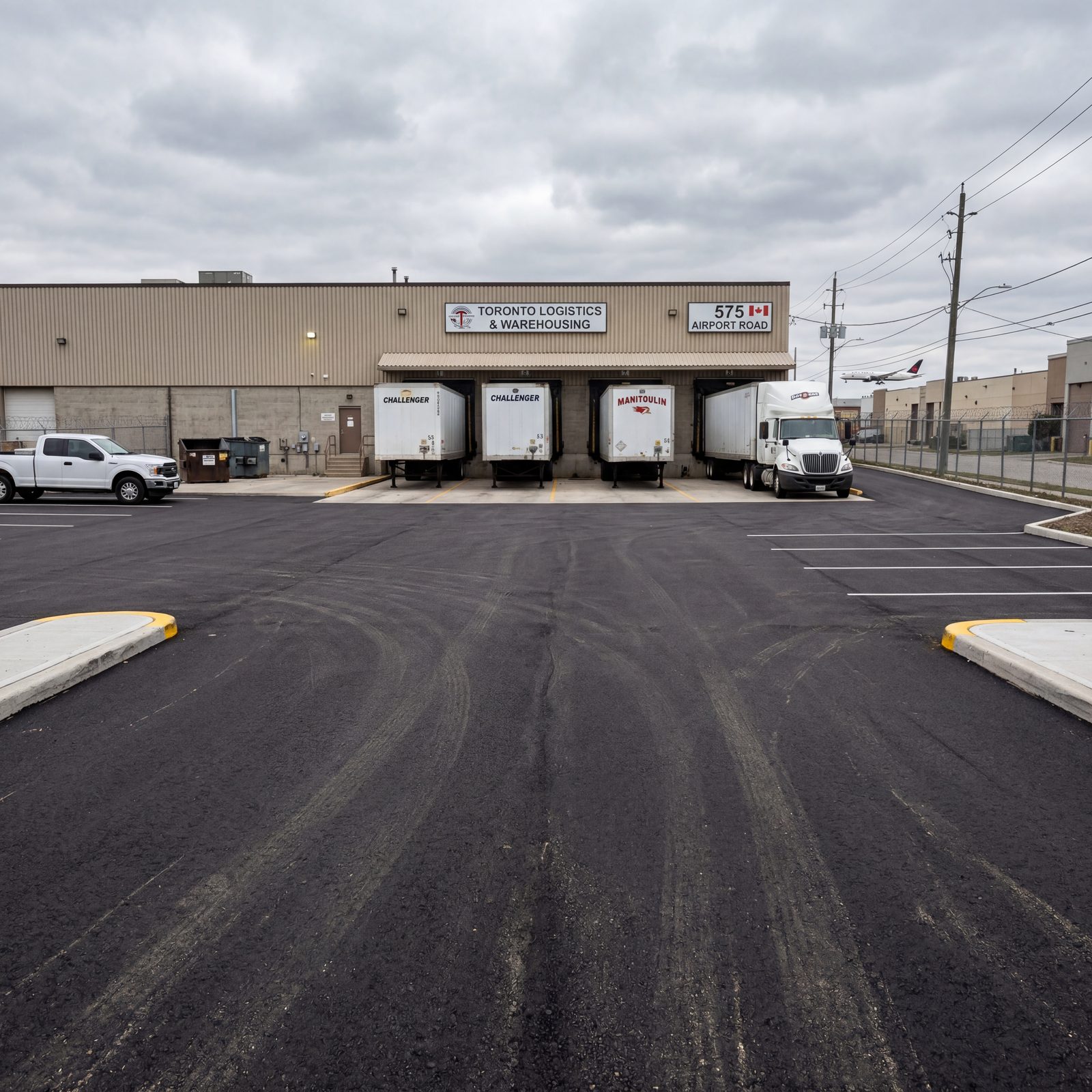 Newly paved asphalt parking and loading dock area with striping and concrete curbs at a Toronto GTA logistics warehouse