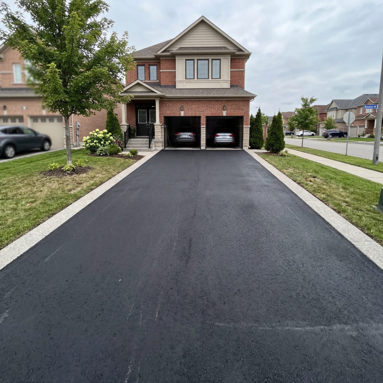 Newly paved black asphalt driveway with concrete border leading to a two-car garage of a GTA home