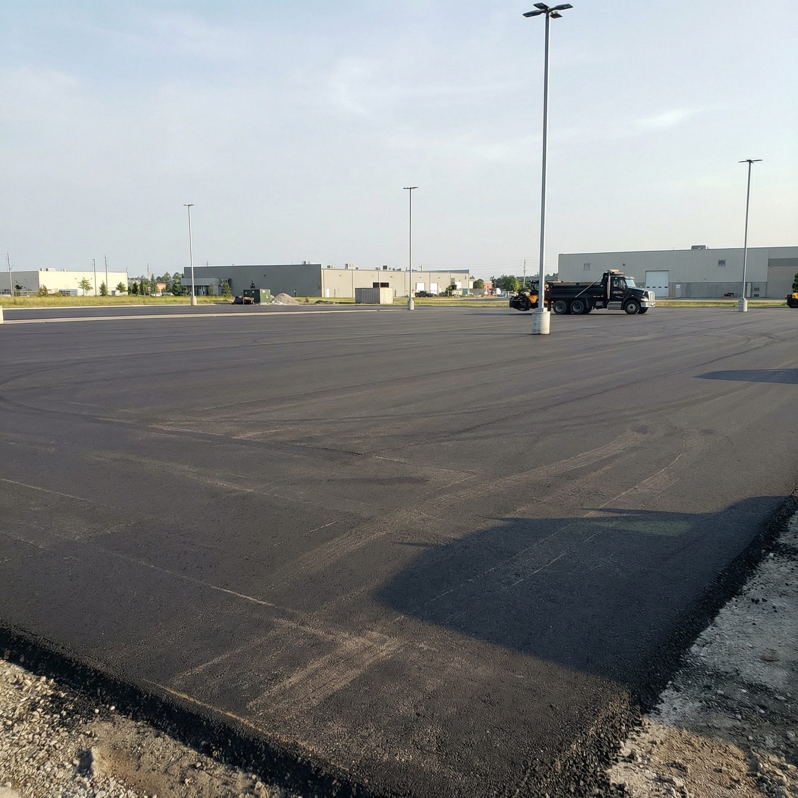 Freshly paved large commercial parking lot with dump truck and industrial buildings in the Greater Toronto Area
