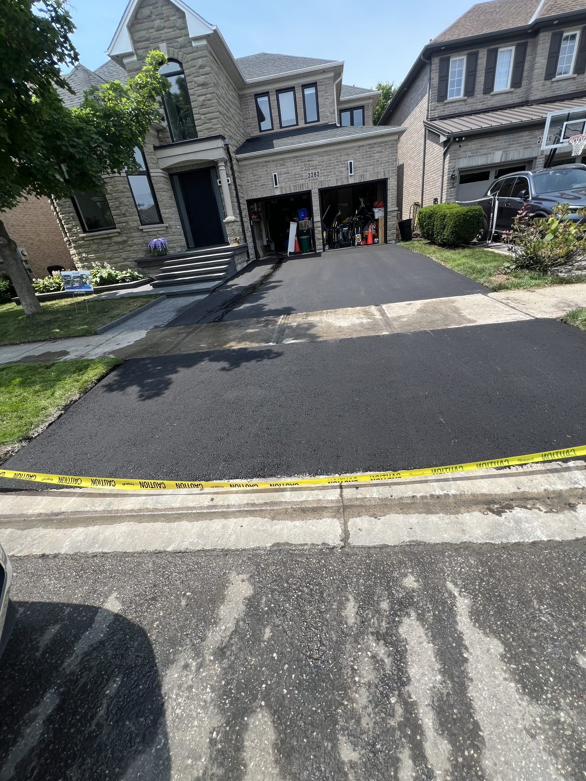Newly paved smooth black asphalt residential driveway with caution tape in front of a stone home in the GTA