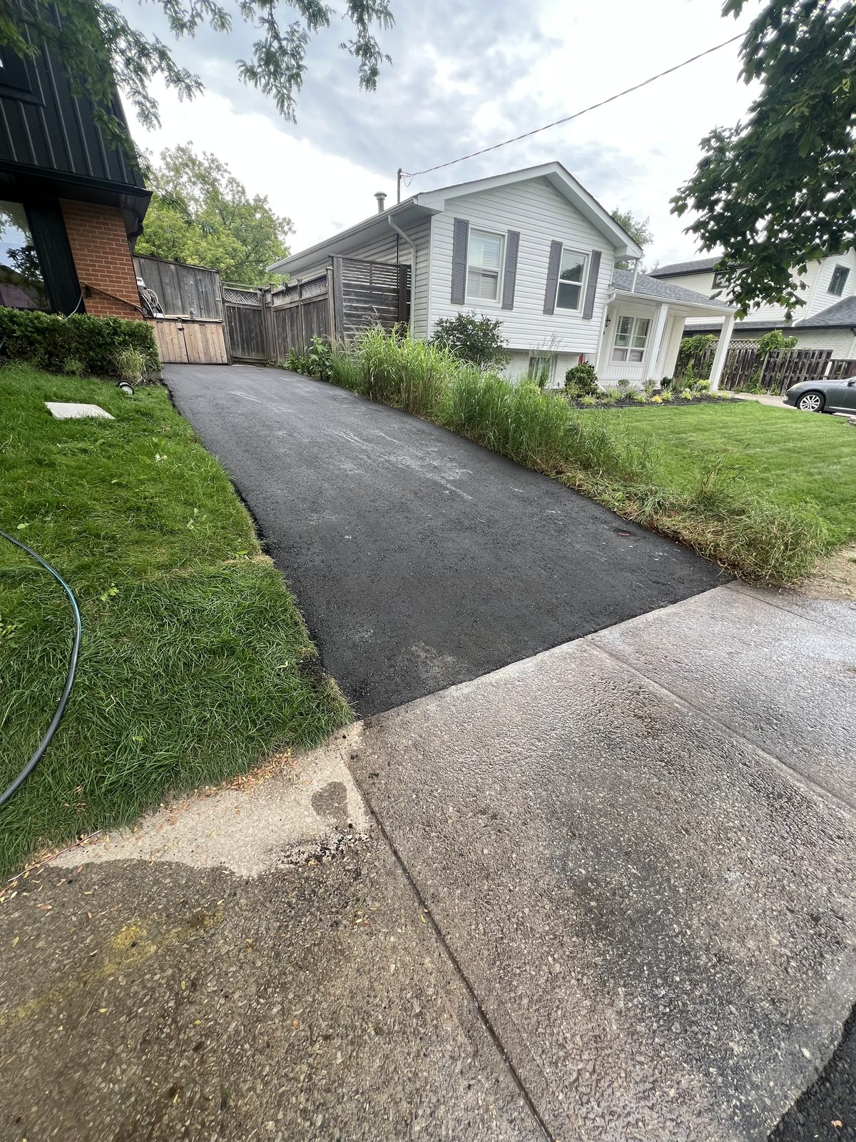 Freshly paved asphalt driveway with clean edges leading to a suburban home in the GTA, bordered by green lawn and concrete apron