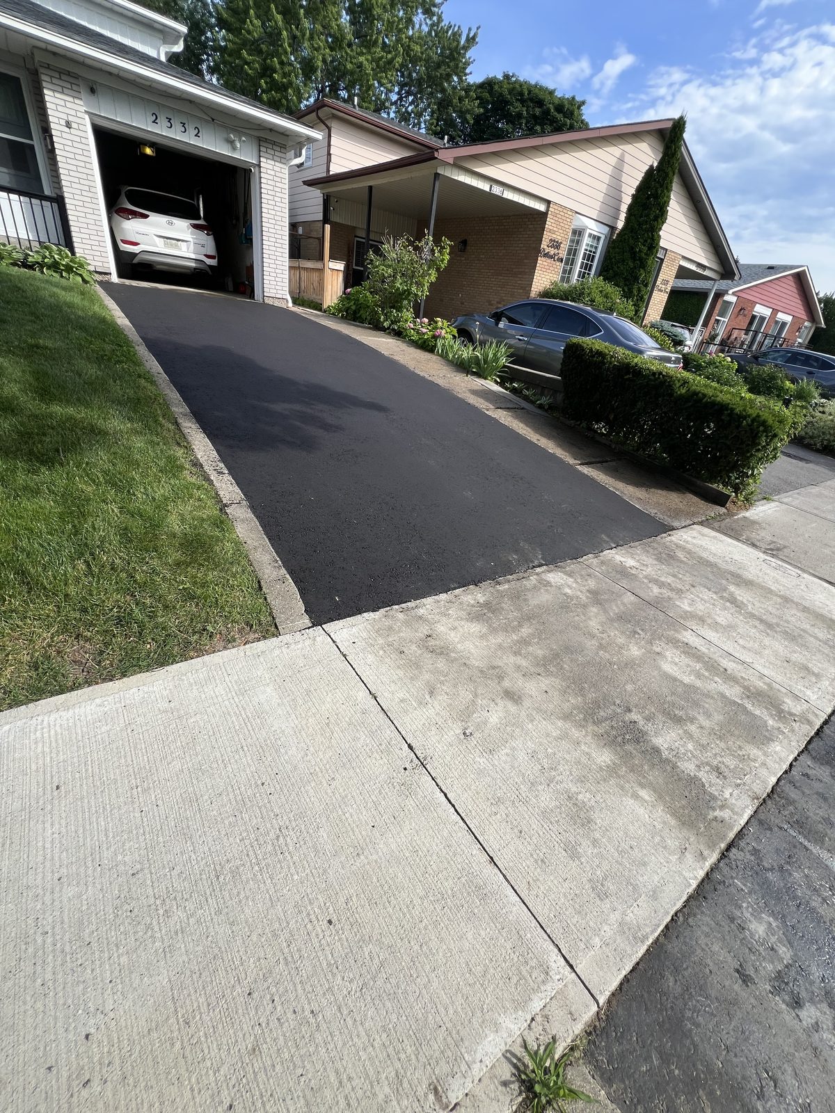 Newly paved smooth black asphalt driveway leading to a garage at a GTA home with concrete sidewalk and manicured lawn