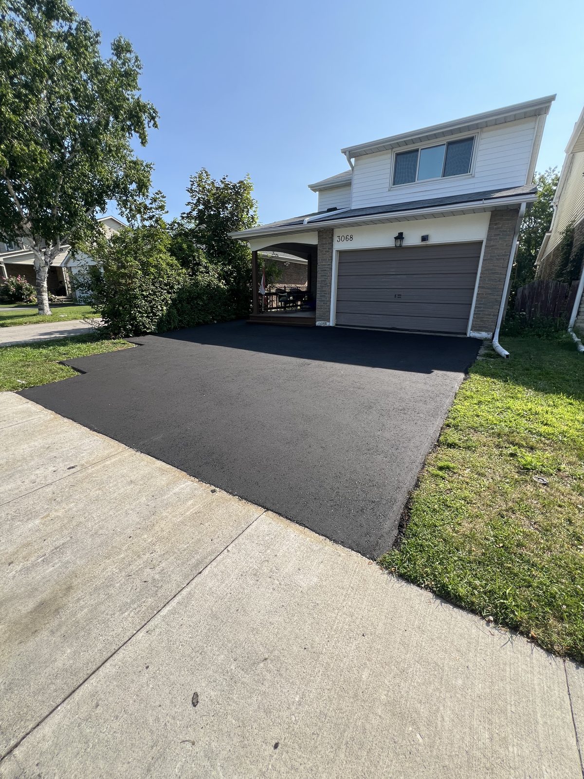 Newly paved smooth black asphalt driveway leading to a two-story home's garage in the GTA