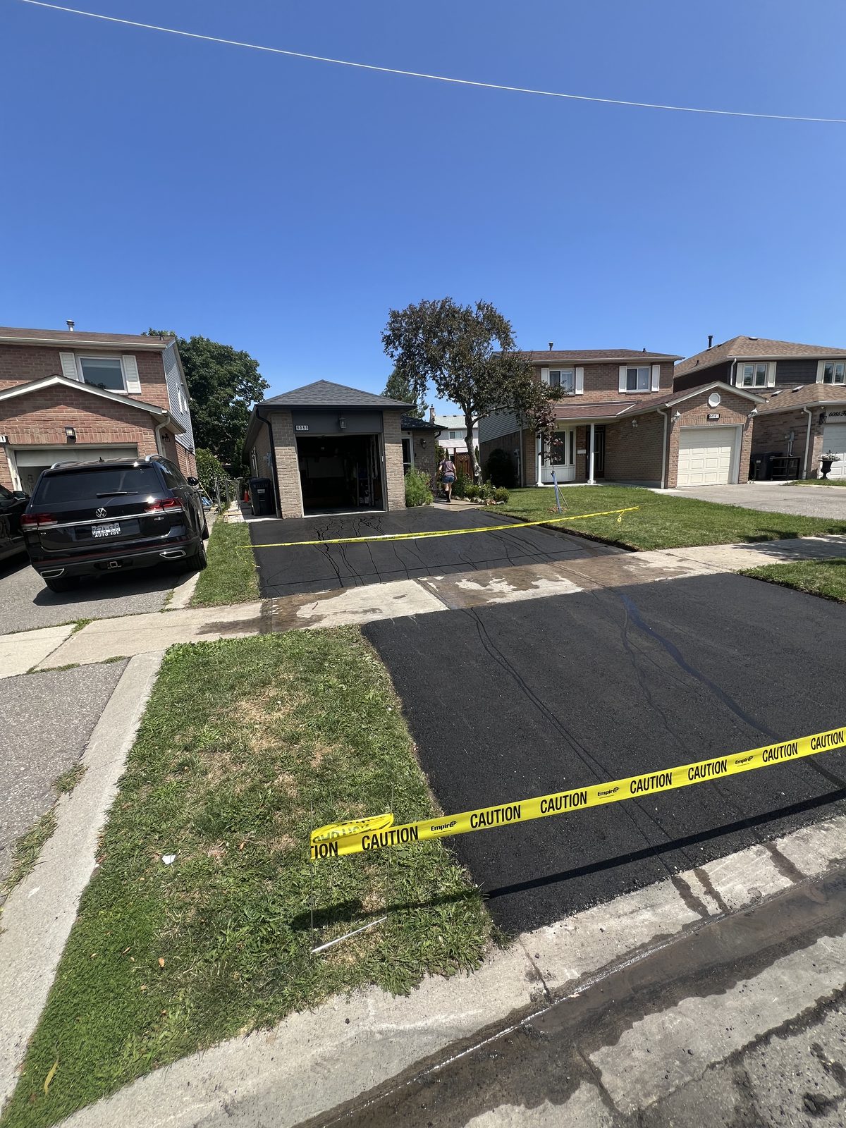 Newly paved black asphalt driveway with caution tape at a suburban brick home in the Greater Toronto Area