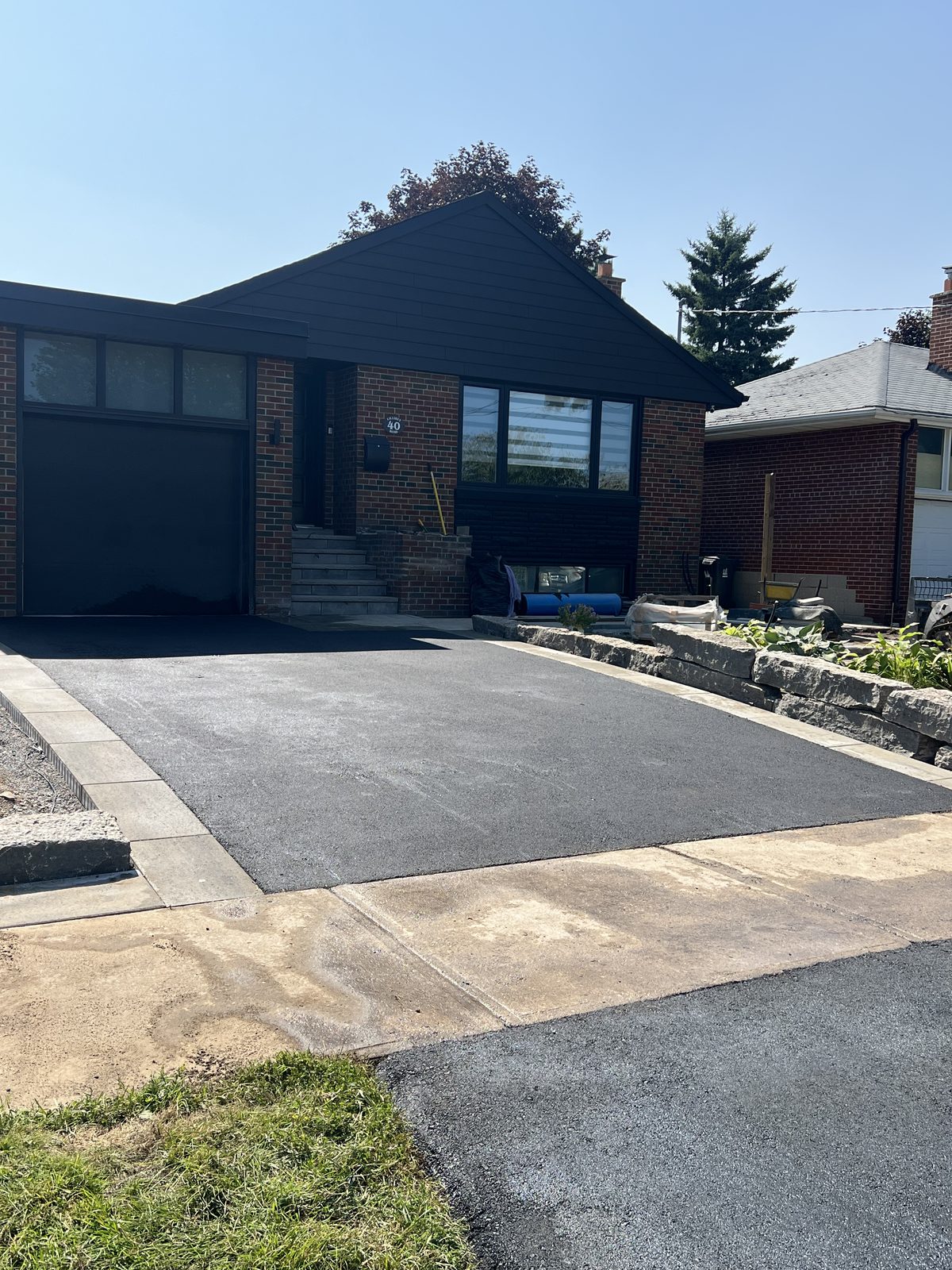 Newly paved asphalt driveway with paver edging leading to a black garage at a GTA residential home
