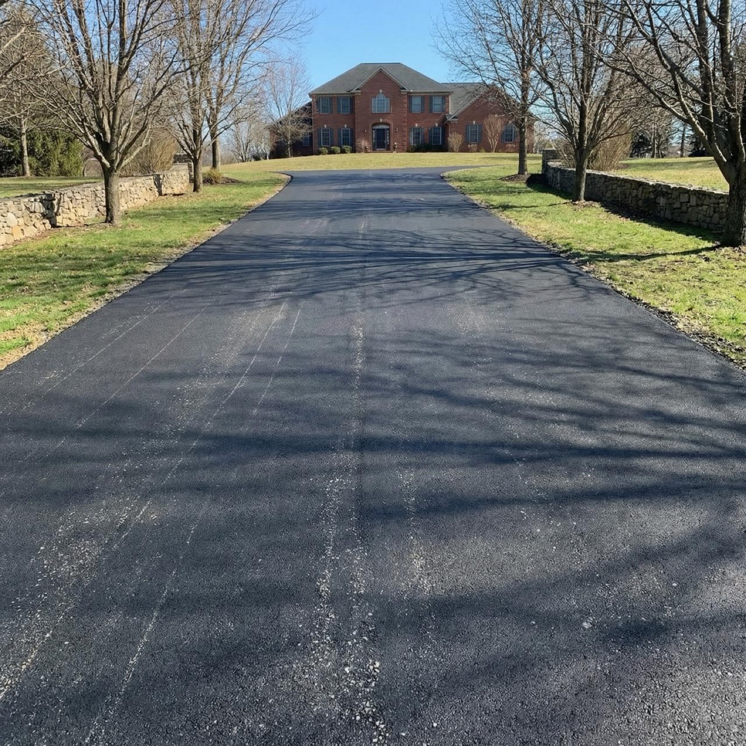 Long estate asphalt driveway leading to a large home, freshly paved